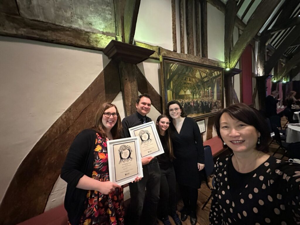 Members of the Disability Inclusion Toolkit Team collecting the award at the Inclusive Impact Awards Ceremony - they are smiling, smartly dressed and in a medieval timbered hall. 